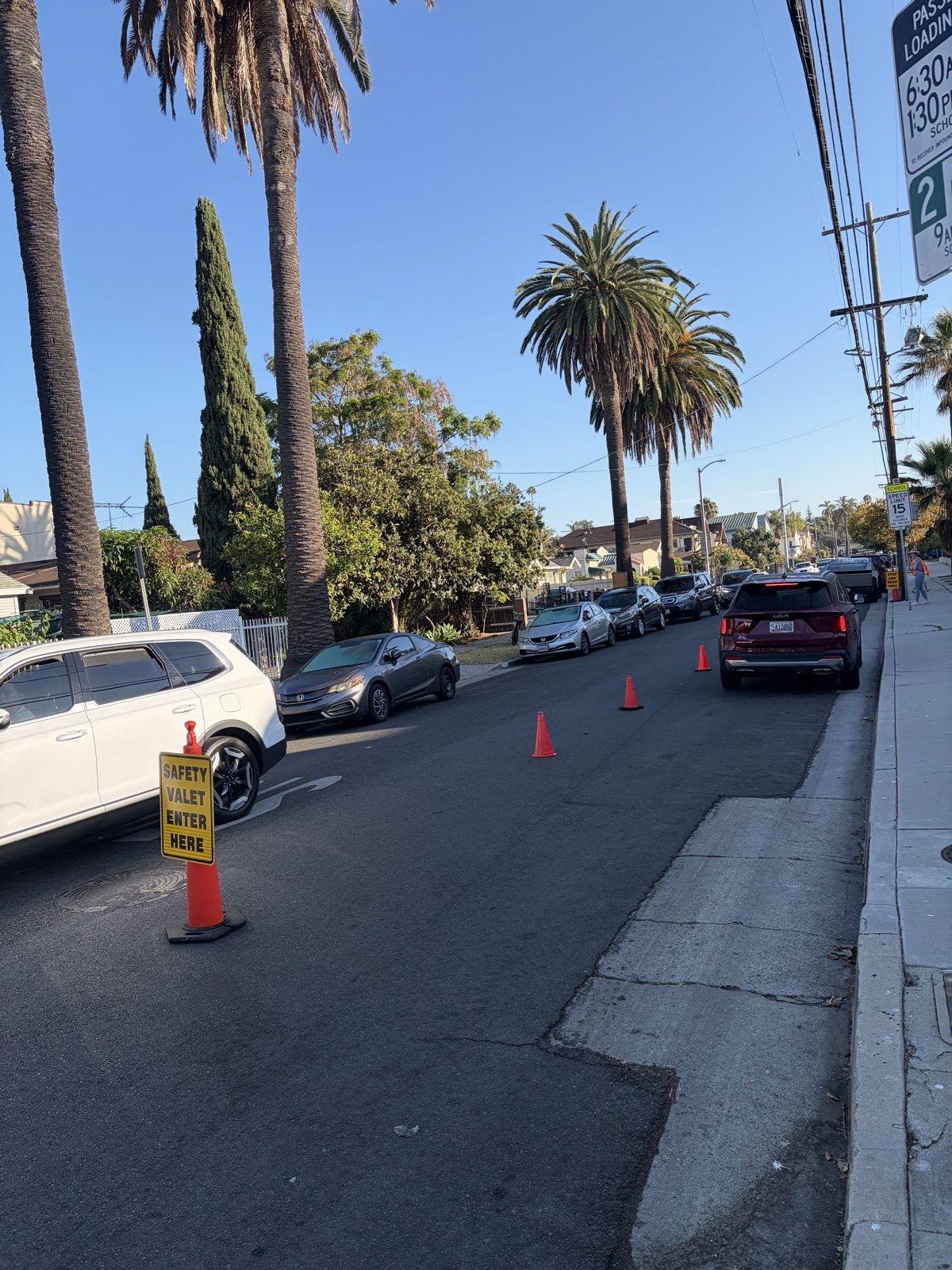 A yellow sign reading Safety Valet Enter Here mounted on an orange cone at the start of the block